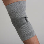 Gray elbow brace on a person's arm with a blue shirt and outdoor background