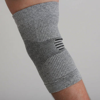 Gray elbow brace on a person's arm with a blue shirt and outdoor background