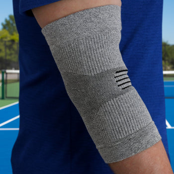 Gray elbow brace on a person's arm with a blue shirt and outdoor background